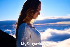 Qué busca una Sugar Baby: Decisiones En la imagen podemos ver a una mujer joven de perfil. Es joven y muy atractiva. Podría ser una Sugar Baby. En el fondo se ve un paisaje hermoso. Un horizonte extenso lleno de nubes. ¿Qué es lo que busca una Sugar Baby? ¿Cuáles son sus motivos? Esta imagen representa el momento pensativo.
